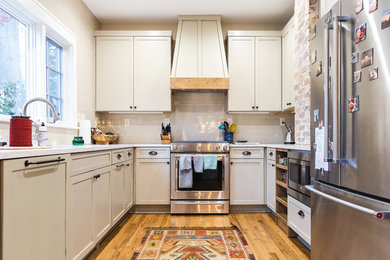 Example of a transitional u-shaped medium tone wood floor and brown floor kitchen design in Other with an undermount sink, recessed-panel cabinets, beige cabinets, beige backsplash, stainless steel appliances and white countertops