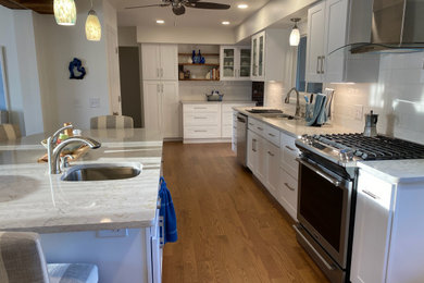 Huge trendy u-shaped medium tone wood floor and brown floor eat-in kitchen photo in Other with an undermount sink, shaker cabinets, white cabinets, quartz countertops, white backsplash, ceramic backsplash, stainless steel appliances, an island and white countertops