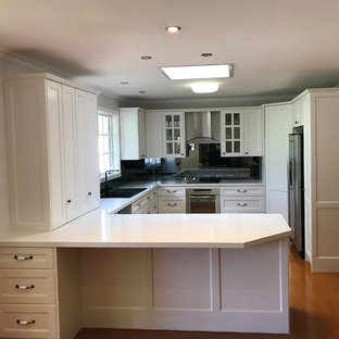 Mid-sized country u-shaped kitchen pantry in Melbourne with a double-bowl sink, recessed-panel cabinets, white cabinets, quartz benchtops, glass sheet splashback, stainless steel appliances, cork floors and with island.