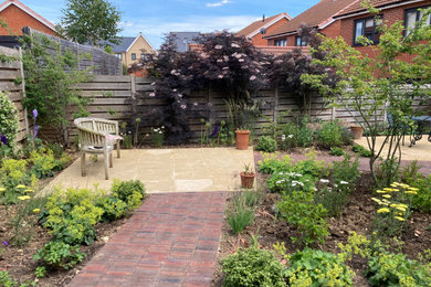 This is an example of a small contemporary back partial sun garden for summer in Cambridgeshire with a flowerbed, brick paving and a wood fence.