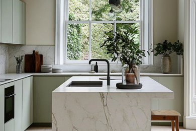 Inspiration for a medium sized classic l-shaped open plan kitchen in London with a built-in sink, flat-panel cabinets, green cabinets, marble worktops, white splashback, marble splashback, black appliances, light hardwood flooring, an island, white worktops and a drop ceiling.