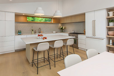 Example of a mid-sized trendy l-shaped light wood floor open concept kitchen design in Detroit with an undermount sink, flat-panel cabinets, white cabinets, quartz countertops, green backsplash, ceramic backsplash, paneled appliances, an island and white countertops