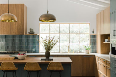 Midcentury l-shaped kitchen in Los Angeles with flat-panel cabinets, medium wood cabinets, blue splashback, with island, grey floor, white benchtop, exposed beam and vaulted.