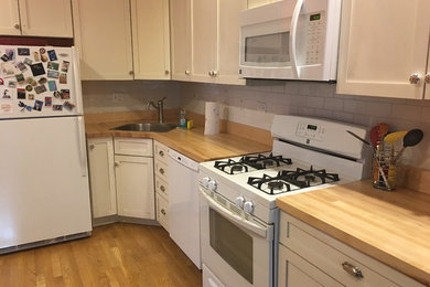 Mid-sized country l-shaped light wood floor and brown floor eat-in kitchen photo in Chicago with an undermount sink, shaker cabinets, white cabinets, wood countertops, white backsplash, subway tile backsplash, white appliances and no island