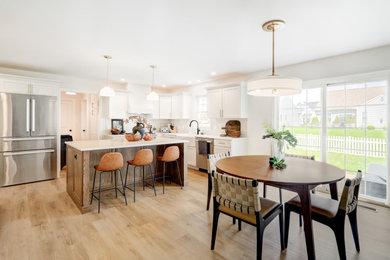 Example of a huge trendy u-shaped vinyl floor and brown floor open concept kitchen design in Other with a farmhouse sink, recessed-panel cabinets, white cabinets, quartz countertops, white backsplash, subway tile backsplash, stainless steel appliances, an island and white countertops