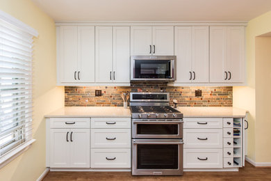 Example of a mid-sized transitional u-shaped vinyl floor and brown floor eat-in kitchen design in DC Metro with an undermount sink, shaker cabinets, white cabinets, quartz countertops, gray backsplash, stone tile backsplash, stainless steel appliances, a peninsula and beige countertops