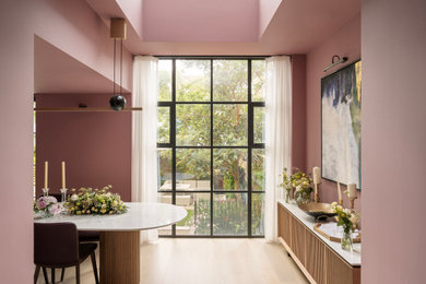 This is an example of a large contemporary enclosed dining room in London with pink walls, light hardwood flooring and feature lighting.
