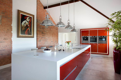 Photo of a large contemporary l-shaped enclosed kitchen in Belfast with a submerged sink, flat-panel cabinets, orange cabinets, composite countertops, white splashback, stone slab splashback, stainless steel appliances, ceramic flooring, an island and grey floors.