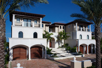 This is an example of a large mediterranean three-storey white house exterior in Tampa with stone veneer, a hip roof and a tile roof.