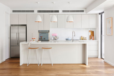 Design ideas for a contemporary single-wall open plan kitchen in Other with an undermount sink, flat-panel cabinets, beige cabinets, white splashback, stainless steel appliances, light hardwood floors, with island, beige floor, quartz benchtops and glass sheet splashback.
