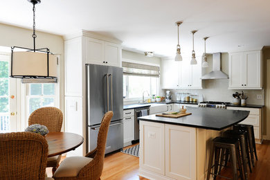 Inspiration for a mid-sized beach style l-shaped eat-in kitchen in DC Metro with a farmhouse sink, shaker cabinets, white cabinets, granite benchtops, grey splashback, ceramic splashback, stainless steel appliances, medium hardwood floors and with island.