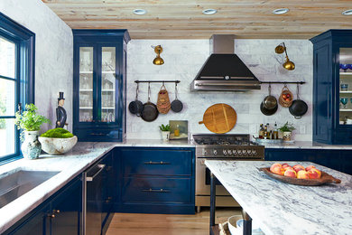 Elegant u-shaped light wood floor kitchen photo in Atlanta with an undermount sink, blue cabinets, marble countertops, white backsplash, stone tile backsplash, stainless steel appliances, an island and glass-front cabinets