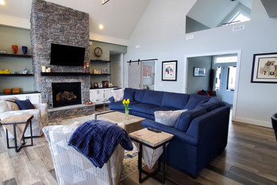 Example of a mid-sized transitional open concept ceramic tile, gray floor and vaulted ceiling family room design in Other with gray walls, a standard fireplace, a stacked stone fireplace and a wall-mounted tv
