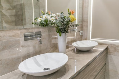 Photo of a medium sized contemporary ensuite bathroom in Brisbane with freestanding cabinets, beige cabinets, a freestanding bath, a double shower, a one-piece toilet, beige tiles, ceramic tiles, beige walls, ceramic flooring, a vessel sink, engineered stone worktops, beige floors and a hinged door.