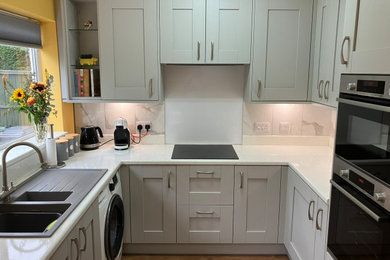 Medium sized contemporary u-shaped kitchen in West Midlands with white splashback, black appliances, laminate floors, no island, brown floors, grey worktops and feature lighting.
