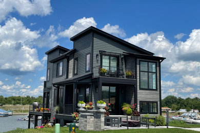 Esempio della facciata di una casa moderna a tre piani con rivestimento con lastre in cemento, copertura a scandole, tetto nero e pannelli sovrapposti