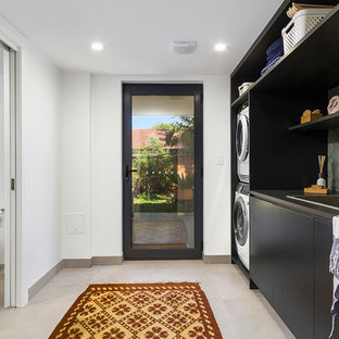 ウロンゴンのコンテンポラリースタイルのおしゃれな洗濯室 (ドロップインシンク、フラットパネル扉のキャビネット、黒いキャビネット、白い壁、上下配置の洗濯機・乾燥機、グレーの床、黒いキッチンカウンター) の写真