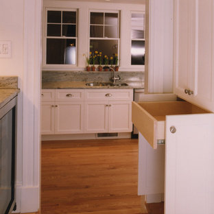 Cette image montre une arrière-cuisine craftsman en L avec un évier encastré, un placard à porte affleurante, des portes de placard blanches, un plan de travail en granite, une crédence en dalle de pierre, un électroménager en acier inoxydable et un sol en bois brun.