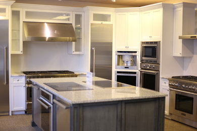 Modelo de cocina actual con puertas de armario blancas, encimera de granito, salpicadero blanco, electrodomésticos de acero inoxidable y una isla