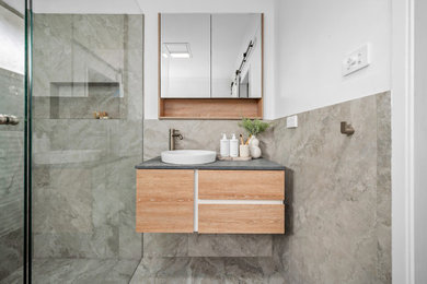Design ideas for a mid-sized beach style kids bathroom in Newcastle - Maitland with flat-panel cabinets, light wood cabinets, a freestanding tub, a corner shower, gray tile, white walls, a vessel sink, grey floor, a hinged shower door, grey benchtops, a niche, a single vanity and a floating vanity.