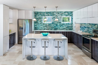 Mid-sized contemporary u-shaped eat-in kitchen in Tampa with a farmhouse sink, flat-panel cabinets, white cabinets, solid surface benchtops, multi-coloured splashback, glass tile splashback, stainless steel appliances, porcelain floors and with island.