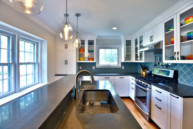 Mid-sized transitional l-shaped light wood floor kitchen pantry photo in New York with an undermount sink, shaker cabinets, white cabinets, quartz countertops, blue backsplash, glass tile backsplash, stainless steel appliances, an island and black countertops