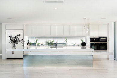 Expansive contemporary galley kitchen in Other with white cabinets, quartz benchtops, black appliances, with island and white benchtop.