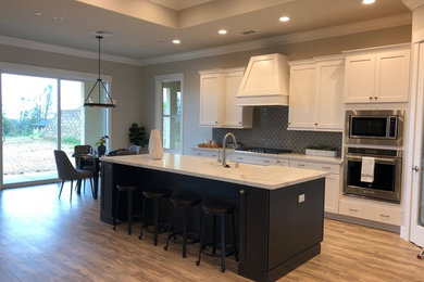 Inspiration for a transitional l-shaped open plan kitchen in Sacramento with a farmhouse sink, white cabinets, glass tile splashback, stainless steel appliances, medium hardwood floors, with island, brown floor, multi-coloured benchtop, shaker cabinets, quartzite benchtops and blue splashback.