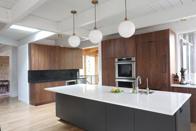 Open concept kitchen - large 1960s l-shaped light wood floor and brown floor open concept kitchen idea in Raleigh with an undermount sink, flat-panel cabinets, medium tone wood cabinets, quartz countertops, black backsplash, stone slab backsplash, paneled appliances, an island and white countertops