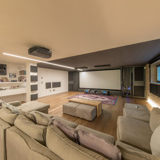 Photo of a large contemporary home cinema in Miami with white walls, a projector screen, light hardwood flooring and beige floors.