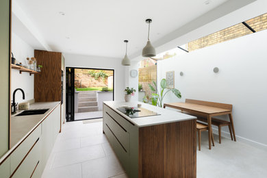 This is an example of a medium sized contemporary galley kitchen/diner in Other with a built-in sink, flat-panel cabinets, green cabinets, composite countertops, grey splashback, travertine splashback, black appliances, travertine flooring, an island, beige floors and grey worktops.