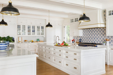 Large beach style open plan kitchen in Milwaukee with a farmhouse sink, recessed-panel cabinets, white cabinets, quartzite benchtops, blue splashback, ceramic splashback, panelled appliances, medium hardwood floors, multiple islands, multi-coloured benchtop and exposed beam.