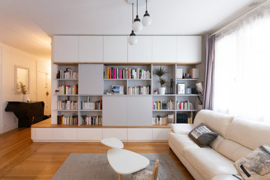 Imagen de biblioteca en casa abierta actual grande sin chimenea con paredes blancas, suelo de madera clara y televisor retractable
