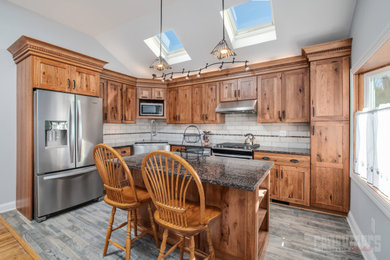 Photo of a mid-sized country l-shaped eat-in kitchen in New York with shaker cabinets, medium wood cabinets, granite benchtops, white splashback, with island, brown benchtop, a farmhouse sink and grey floor.