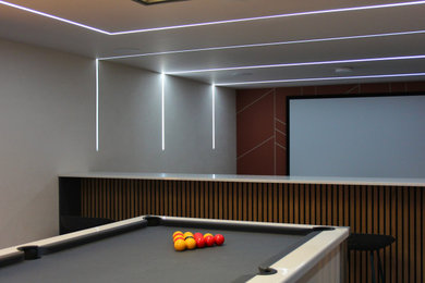 Modelo de sala de juegos en casa abierta minimalista grande con televisor colgado en la pared, suelo azul y panelado