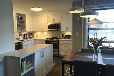 Example of a mid-sized transitional l-shaped black floor eat-in kitchen design in New York with shaker cabinets, white cabinets, solid surface countertops, white backsplash, subway tile backsplash, stainless steel appliances, no island and white countertops