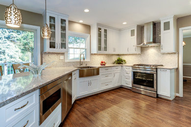 Eat-in kitchen - mid-sized traditional u-shaped medium tone wood floor and brown floor eat-in kitchen idea in DC Metro with a farmhouse sink, shaker cabinets, white cabinets, granite countertops, gray backsplash, stone slab backsplash, stainless steel appliances and a peninsula