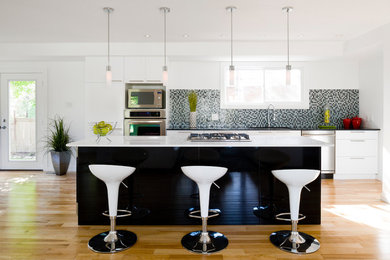 Example of a large transitional galley light wood floor open concept kitchen design in Ottawa with an undermount sink, flat-panel cabinets, white cabinets, quartz countertops, multicolored backsplash, glass tile backsplash, stainless steel appliances and an island