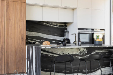 Idées déco pour une grande cuisine linéaire et encastrable contemporaine avec un évier intégré, un placard avec porte à panneau encastré, des portes de placard blanches, un plan de travail en granite, une crédence noire, une crédence en granite, un sol en carrelage de céramique, îlot, un sol beige et plan de travail noir.