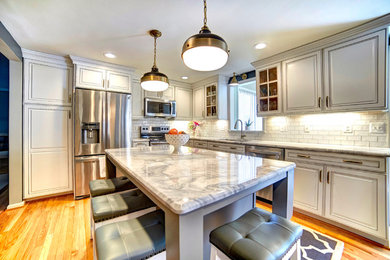 Example of a mid-sized transitional l-shaped light wood floor enclosed kitchen design in Baltimore with a single-bowl sink, raised-panel cabinets, white cabinets, white backsplash, subway tile backsplash, stainless steel appliances and an island