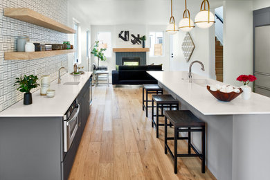 Mid-sized trendy galley light wood floor eat-in kitchen photo in Denver with a double-bowl sink, flat-panel cabinets, gray cabinets, quartz countertops, white backsplash, ceramic backsplash, stainless steel appliances, an island and white countertops