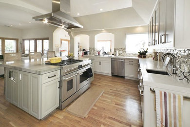 Inspiration for a large transitional u-shaped open plan kitchen in San Francisco with an undermount sink, recessed-panel cabinets, white cabinets, solid surface benchtops, multi-coloured splashback, mosaic tile splashback, stainless steel appliances, medium hardwood floors, with island, brown floor and white benchtop.
