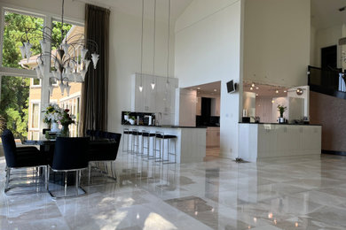 Eat-in kitchen - huge contemporary l-shaped marble floor and white floor eat-in kitchen idea in Charlotte with an undermount sink, flat-panel cabinets, white cabinets, granite countertops, black backsplash, granite backsplash, paneled appliances, an island and black countertops