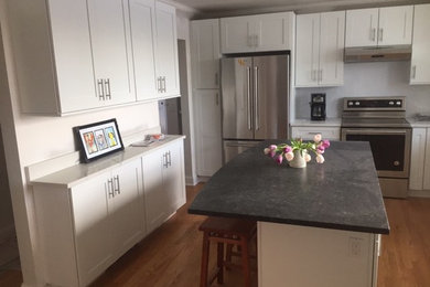 Example of a medium tone wood floor kitchen design in New York with shaker cabinets, white cabinets, granite countertops, stainless steel appliances and an island
