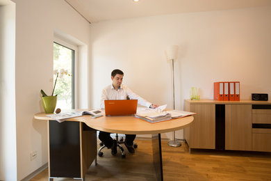 Geräumiges Modernes Arbeitszimmer mit Arbeitsplatz, weißer Wandfarbe, gebeiztem Holzboden und freistehendem Schreibtisch in Berlin