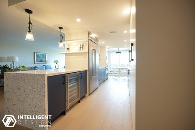 Example of a galley light wood floor and brown floor eat-in kitchen design in Toronto with an undermount sink, flat-panel cabinets, blue cabinets, quartz countertops, white backsplash, ceramic backsplash, stainless steel appliances, a peninsula and gray countertops
