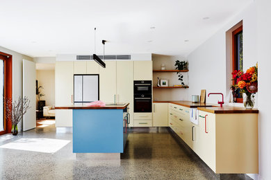Photo of a large eclectic l-shaped open plan kitchen in Sydney with a farmhouse sink, flat-panel cabinets, wood benchtops, black appliances, concrete floors, with island, grey floor and brown benchtop.