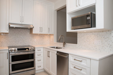 Example of a trendy u-shaped enclosed kitchen design in Vancouver with an undermount sink, recessed-panel cabinets, white cabinets, white backsplash, mosaic tile backsplash, stainless steel appliances, no island and white countertops