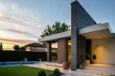 Imagen de fachada de casa multicolor y blanca moderna grande de una planta con revestimiento de piedra, tejado plano, tejado de varios materiales, teja y escaleras