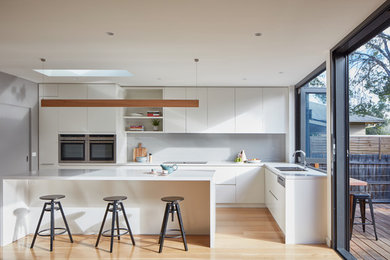 Inspiration for a contemporary l-shaped eat-in kitchen in Melbourne with a double-bowl sink, grey splashback, glass sheet splashback, light hardwood floors, with island and stainless steel appliances.